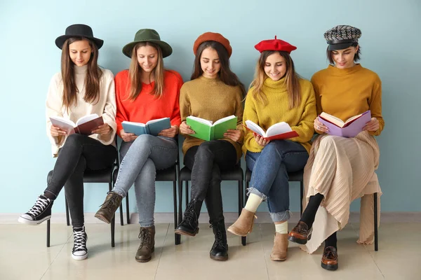 Kitapları olan genç kadınlar renk duvarının yanında oturuyor.