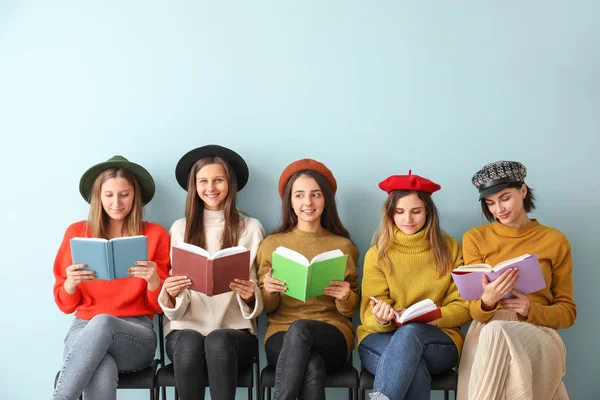 Kitapları olan genç kadınlar renk duvarının yanında oturuyor.