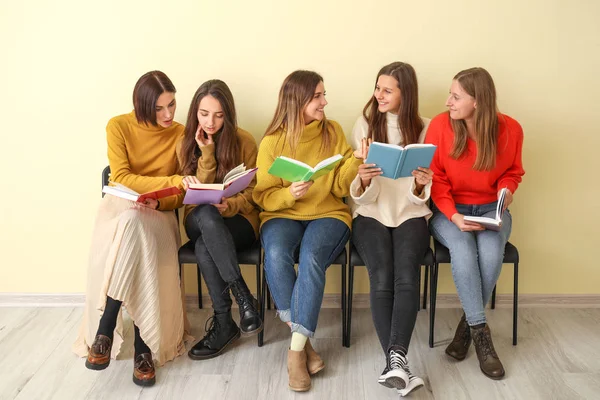 Kitapları olan genç kadınlar renk duvarının yanında oturuyor.