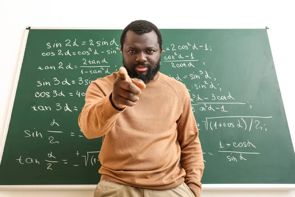 Angry African-American math teacher near blackboard in classroom