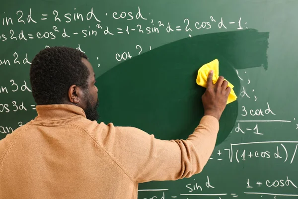 Profesor de matemáticas afroamericano limpiando pizarra en el aula — Foto de Stock