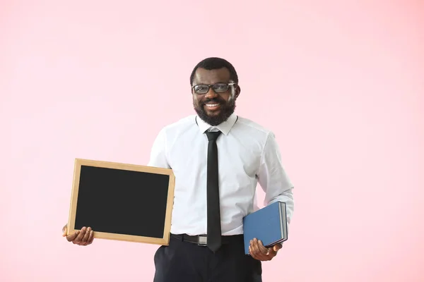 African-American teacher with chalkboard and books on color background — Stock Photo, Image