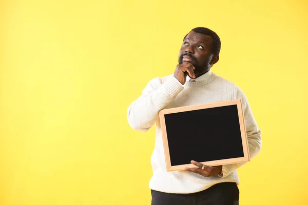 Professor afro-americano cuidadoso com quadro-negro sobre fundo de cor — Fotografia de Stock