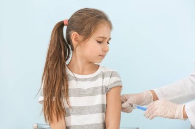 Doktor, küçük kızı ışığa karşı aşılıyor.