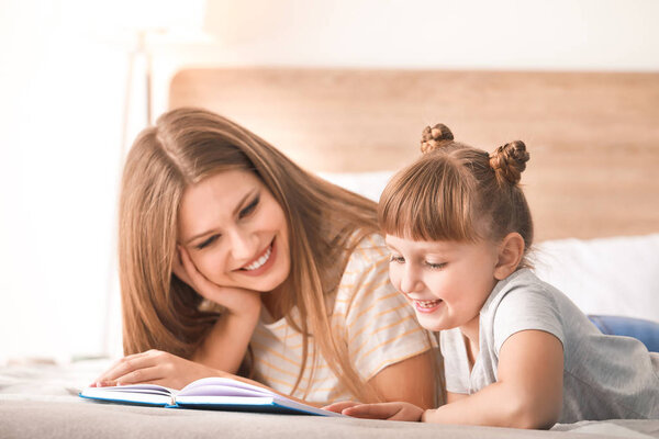 Beautiful young woman and her little daughter reading book at home