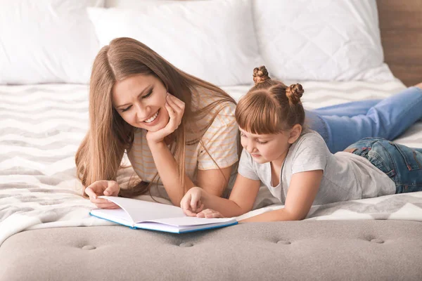 Beautiful young woman and her little daughter reading book at home — Stock Photo, Image