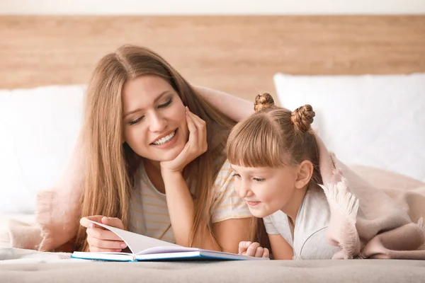 Beautiful young woman and her little daughter reading book at home — 스톡 사진