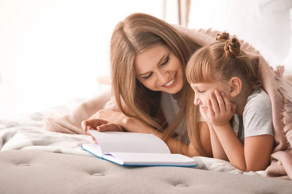 Beautiful young woman and her little daughter reading book at home — Stock Photo, Image