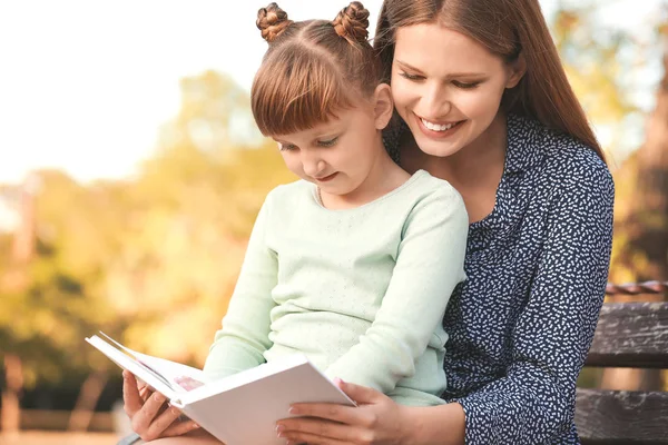 Vacker ung kvinna och hennes lilla dotter läser bok i parken — Stockfoto