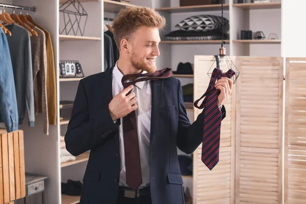 Handsome man choosing necktie in dressing room — Stock Photo, Image