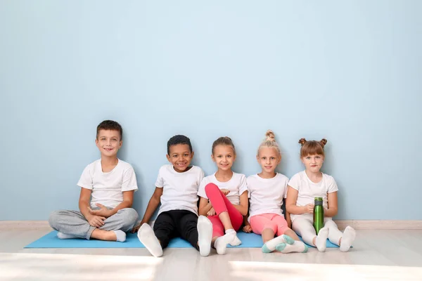 Little children with yoga mats sitting near wall in gym — Stock Photo, Image
