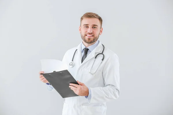 Portrait of male doctor with clipboard on light background — Stock Photo, Image