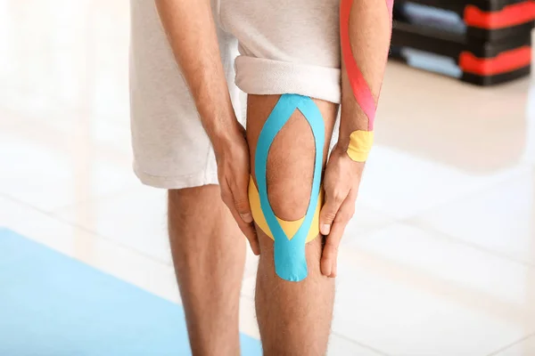 Uomo sportivo con nastro fisioterapico applicato al ginocchio in palestra, primo piano — Foto Stock