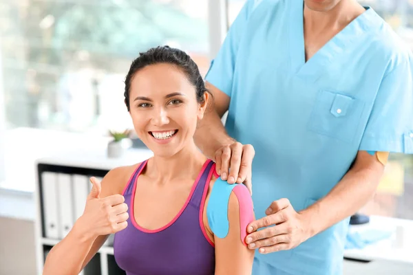 Physiotherapist applying tape onto woman's shoulder in clinic — Stock Photo, Image