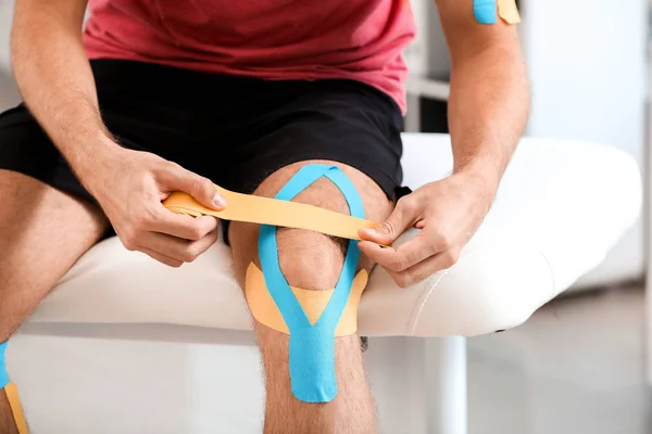 Mężczyzna nakładający taśmę na kolano w klinice — Zdjęcie stockowe