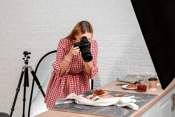 Young woman taking picture of pancakes in professional studio