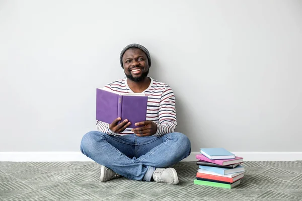 Hombre afroamericano leyendo libro cerca de la pared de luz — Foto de Stock