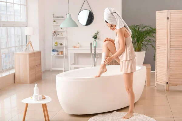 Beautiful young woman shaving legs in bathroom — Stock Photo, Image