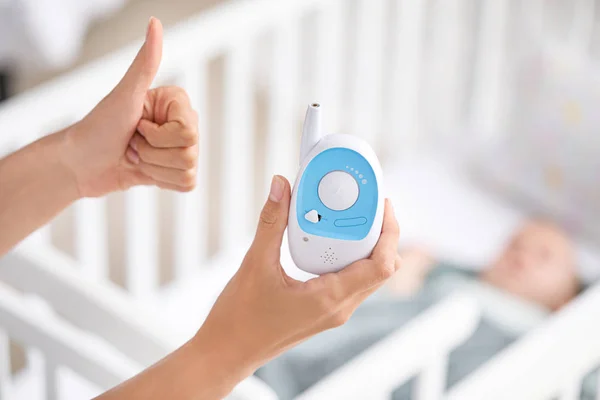 Madre con monitor de bebé moderno mostrando gesto de pulgar hacia arriba cerca de la cama — Foto de Stock