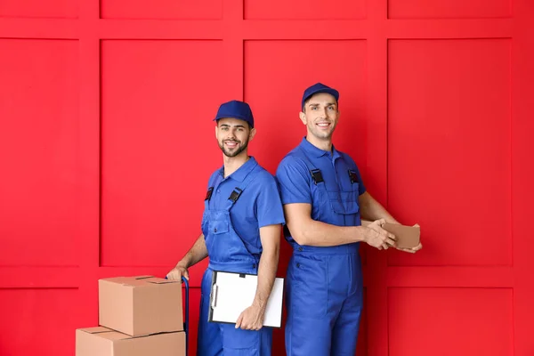 Delivery men with boxes on color background