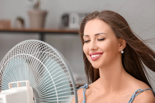 Evde sıcak hava dalgası sırasında elektrikli yelpaze kullanan genç bir kadın. — Stok fotoğraf