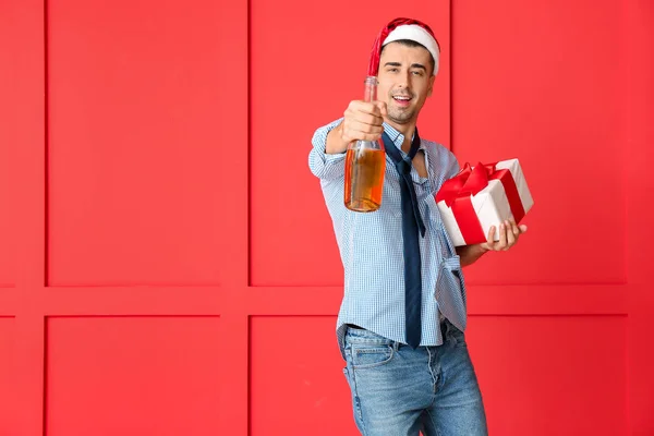 Noel Baba şapkalı sarhoş adam, renk geçmişinde hediye ve şampanya. — Stok fotoğraf