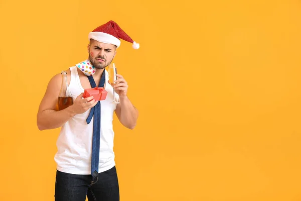 Homme ivre avec chapeau de Père Noël, cadeau et champagne sur fond de couleur — Photo