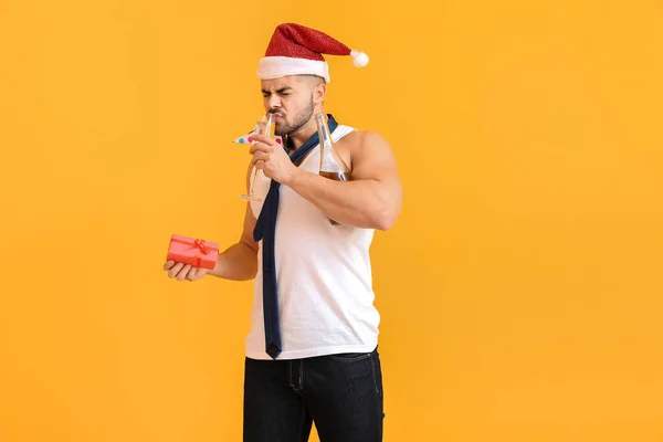 Drunk man with Santa Claus hat, gift and champagne on color background — Stock Photo, Image