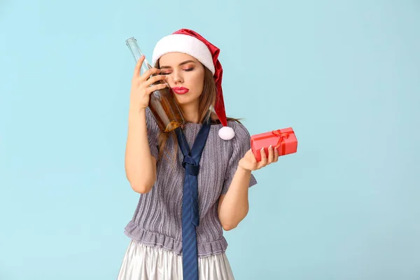 Mujer borracha en sombrero de Santa Claus, con champán y regalo sobre fondo de color —  Fotos de Stock