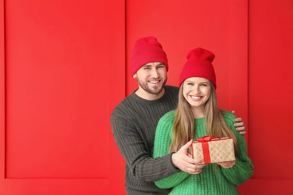 Retrato de pareja feliz en ropa de invierno y con regalo sobre fondo de color — Foto de Stock