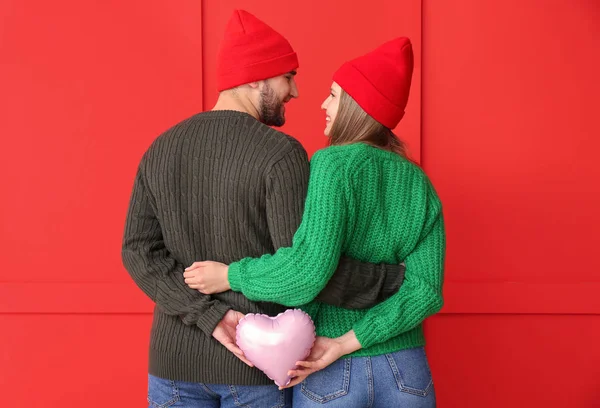 Retrato de pareja feliz en ropa de invierno y con corazón sobre fondo de color — Foto de Stock