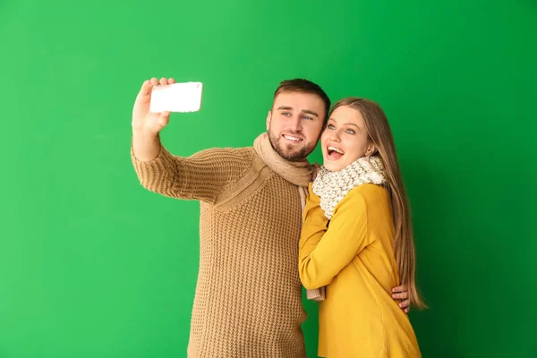 Portrait of happy couple in winter clothes taking selfie on color background — 스톡 사진