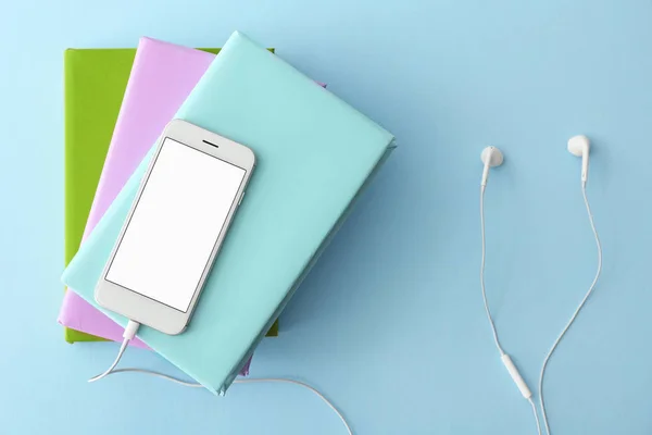 色の背景に本、携帯電話や現代のイヤフォン。オーディオブックの概念 — ストック写真