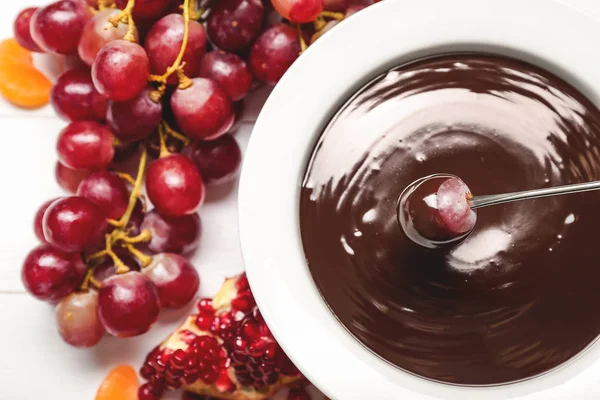 Sumergir la uva sabrosa en un tazón con fondue de chocolate en la mesa — Foto de Stock