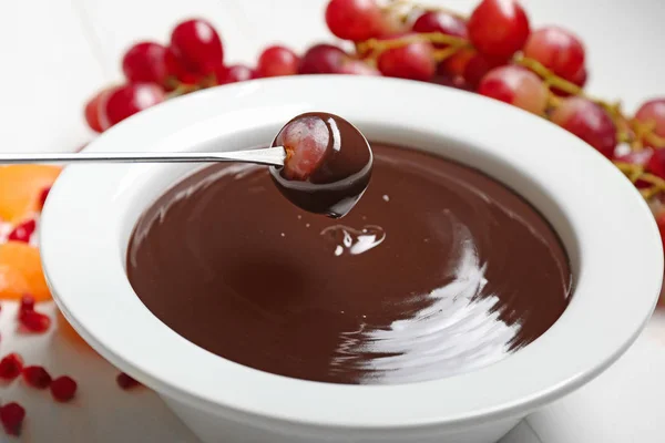 Dipping of tasty grape into bowl with chocolate fondue on table, closeup — Stock Photo, Image