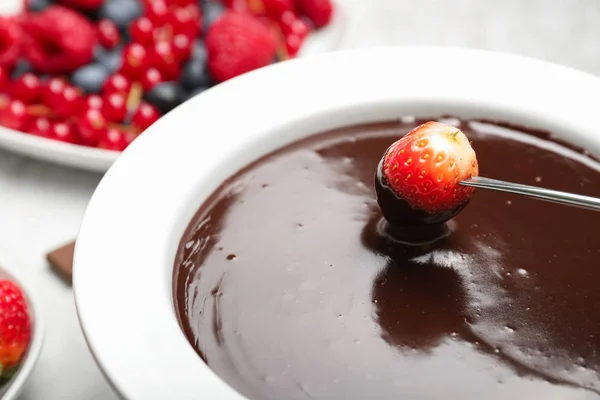 Trempage de fraises savoureuses dans un bol avec fondue au chocolat sur la table, gros plan — Photo