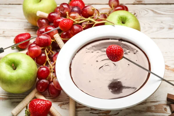 Dipping of tasty strawberry into bowl with chocolate fondue on table — Stock Photo, Image