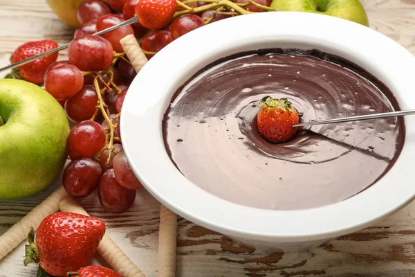 Dipping of tasty strawberry into bowl with chocolate fondue on table — Stock Photo, Image