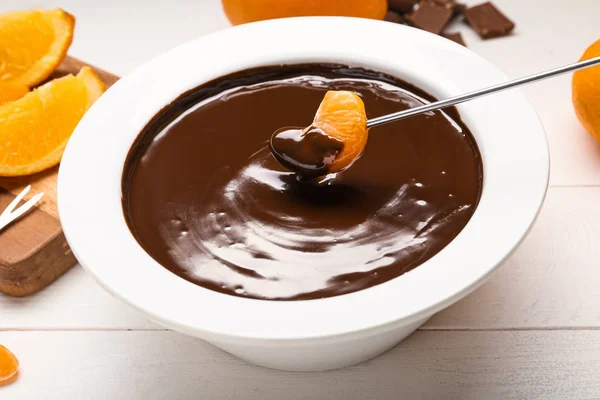 Sumergir la sabrosa mandarina en un tazón con fondue de chocolate en la mesa — Foto de Stock