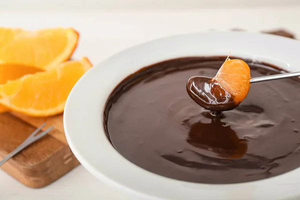 Dipping of tasty tangerine into bowl with chocolate fondue on table, closeup — Stock Photo, Image