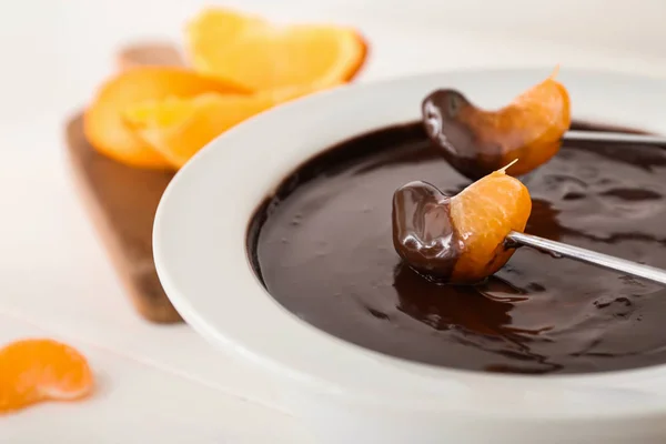 Dipping of tasty tangerine into bowl with chocolate fondue on table, closeup — Stock Photo, Image