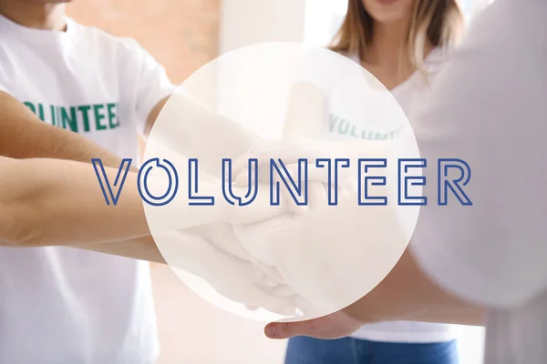 Team of young volunteers putting hands together indoors — Stock Photo, Image