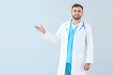 Portrait of male doctor showing something on light background