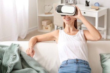 Evde sanal gerçeklik gözlüklü genç bir kadın var.