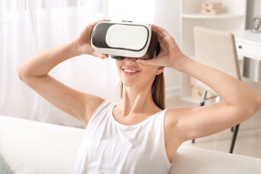 Evde sanal gerçeklik gözlüklü genç bir kadın var.