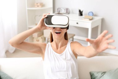 Evde sanal gerçeklik gözlüklü genç bir kadın var.