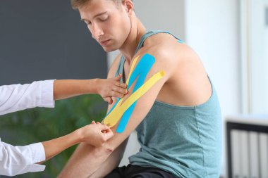 Fizyoterapist klinikteki adamın koluna bant yapıştırıyor.