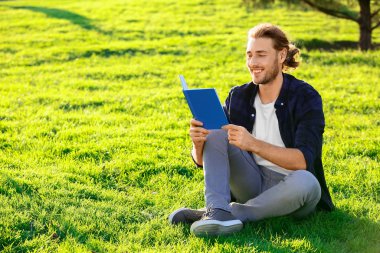 Dışarıda kitap okuyan yakışıklı bir adam.