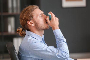 Sick businessman with inhaler in office