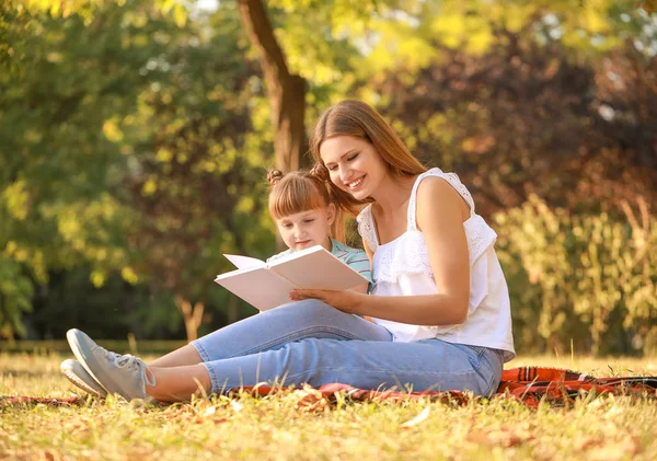 Mulher bonita e sua filhinha lendo livro no parque — Fotografia de Stock